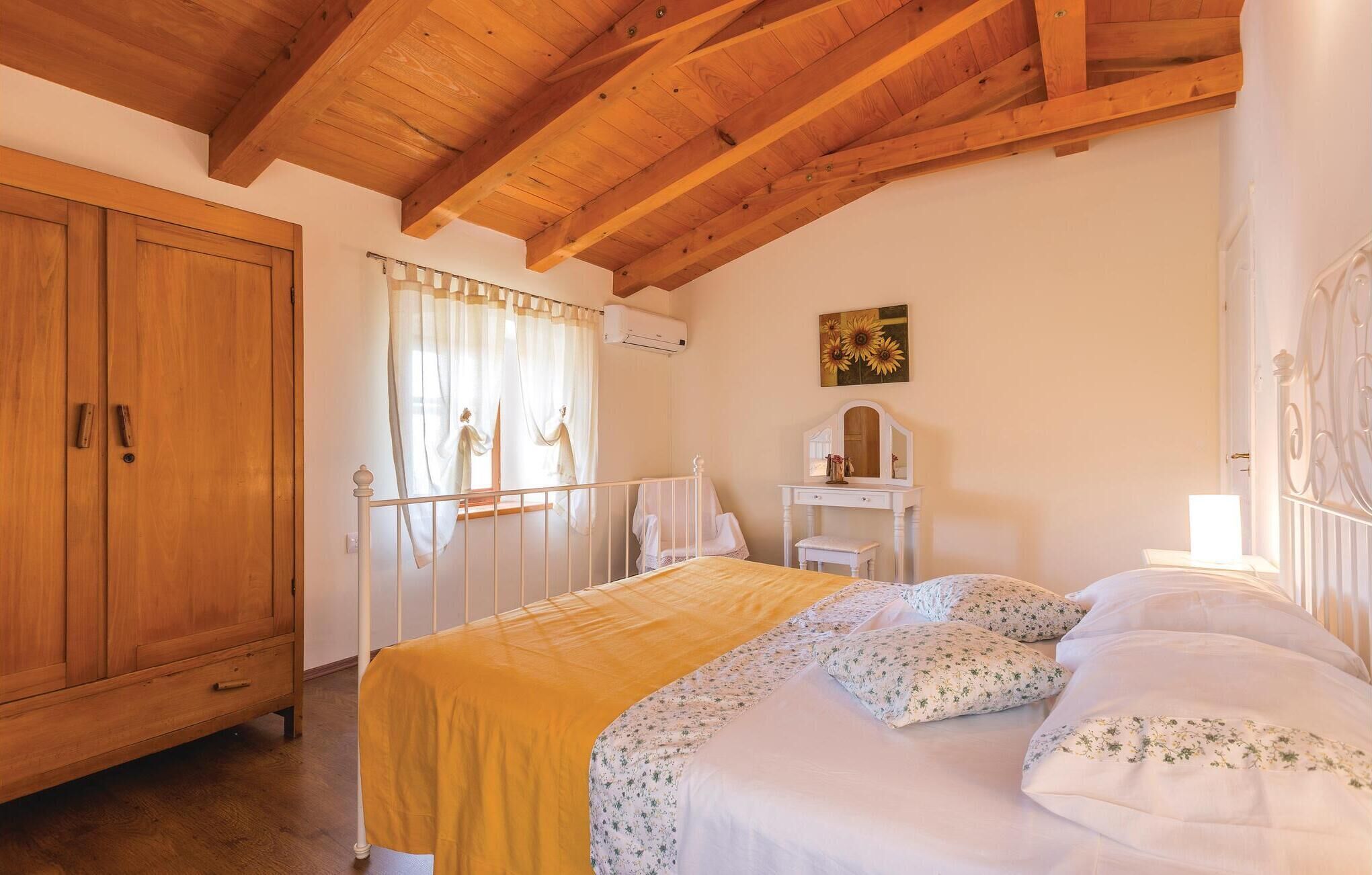 A bedroom with a wooden ceiling, a bed with floral bedding, a nightstand, a dresser, and a window with curtains.