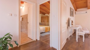 Una habitación con techo de madera, una cama con colcha amarilla, una mesita de noche blanca con espejo y una planta en la esquina.