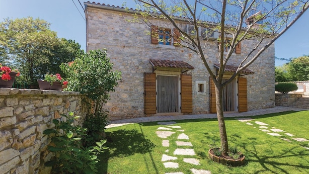 Un edificio de piedra con tejado de baldosas, una puerta de madera y un pequeño jardín con un sendero empedrado.