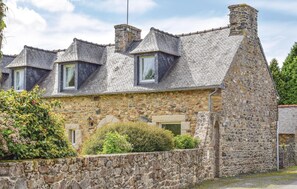 Un bâtiment en pierre doté d’un toit à forte pente, de plusieurs cheminées et d’une petite fenêtre.
