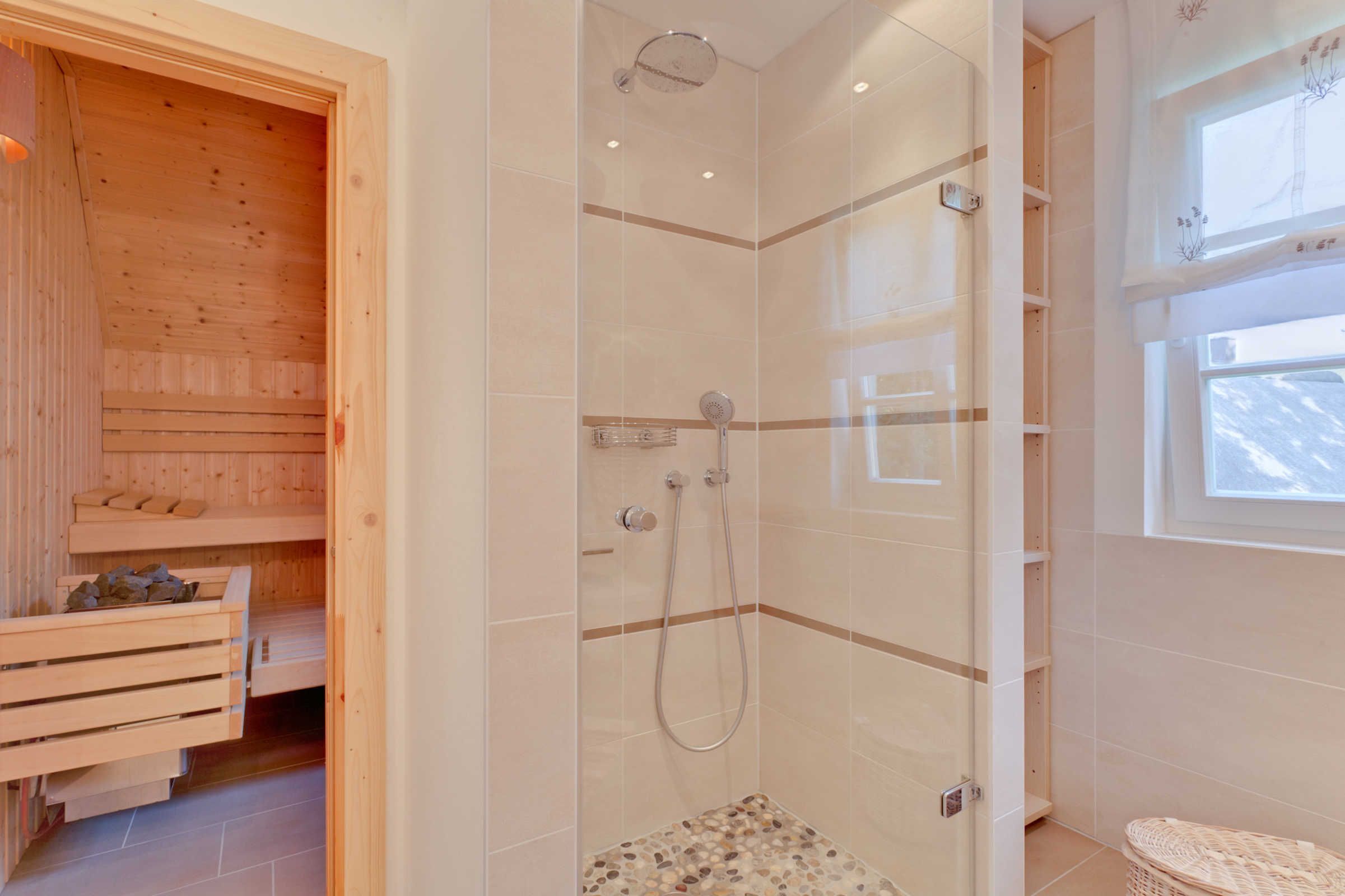 Une salle de bain moderne dotée d’une douche à parois de verre, de bancs en bois pour le sauna et d’une grande fenêtre qui laisse entrer la lumière naturelle.