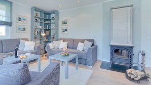 A modern living room with a grey sofa, a coffee table, a bookshelf, and a fireplace. - Aquamaritim beach house (Loddin)
