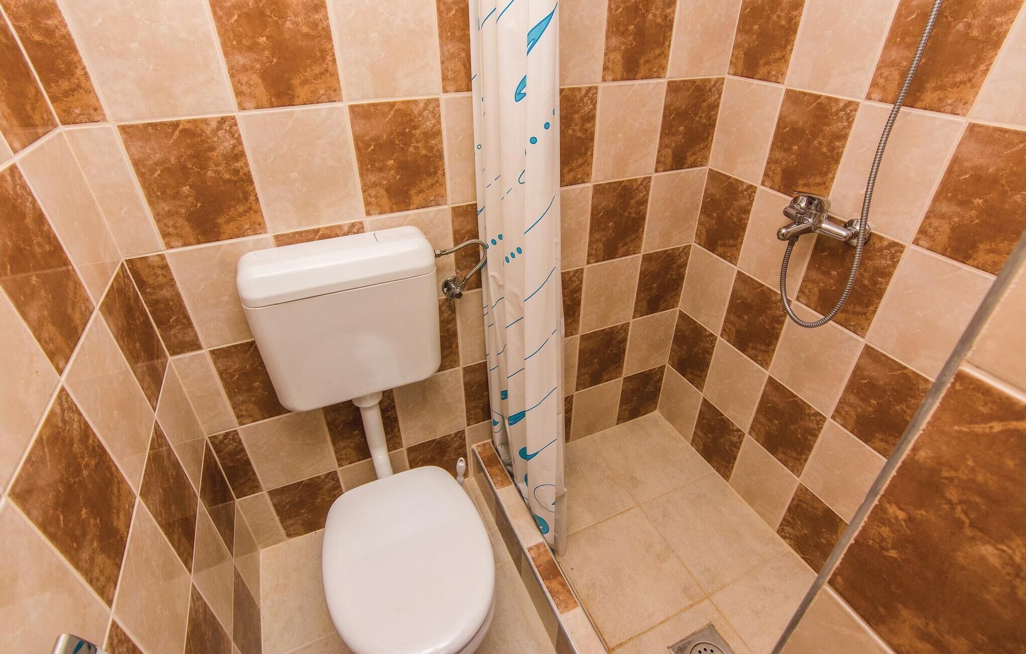 A small, tiled bathroom with a toilet, shower, and a wall-mounted toilet paper holder.