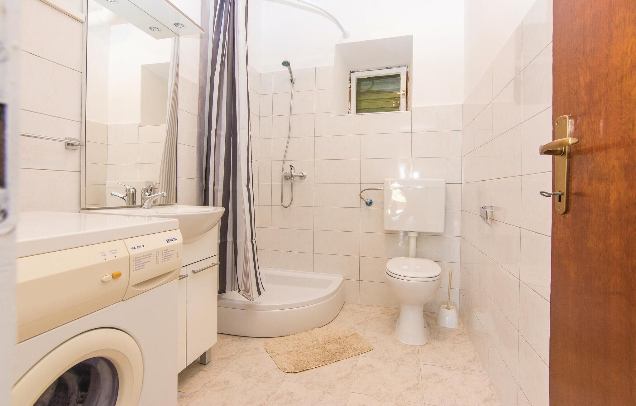 Une petite salle de bain équipée d’un lave-linge, d’un évier, de toilettes et d’une douche.