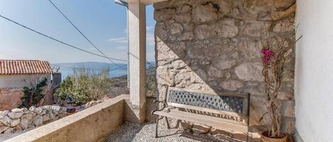 A balcony with a stone wall, a wooden bench, and a potted plant.