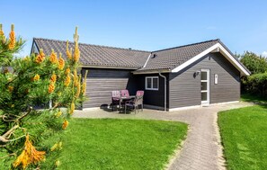 Ett modernt hus med en grå fasad, ett tak täckt med takpannor och en liten veranda med ett bord och några stolar.