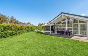 Ett modernt hus med ett stort glashus, en välskött gräsmatta och en möblerad uteplats.