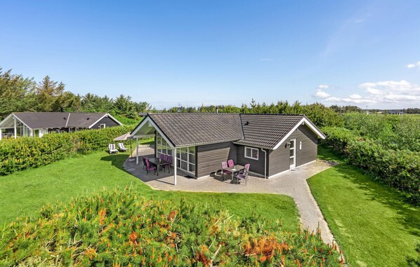 Ett modernt hus med en uteplats, omgivet av frodig grönska och en klar himmel.