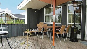 Un patio exterior con terraza de madera, una mesa con sillas y una parrilla.