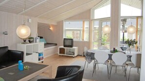 Amplia sala de estar con techos altos, televisor, mesa de comedor con sillas y ventanas grandes que permiten la entrada de luz natural.
