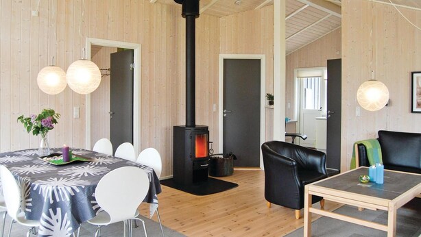 Una habitación acogedora con detalles de madera, una estufa de leña negra, una mesa de comedor con sillas y un sofá.