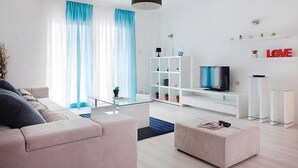 Een moderne woonkamer met een bank, een poef, een televisie en een witte wandplank.