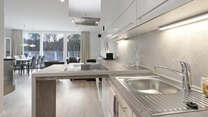 Een moderne keuken met een centraal kookeiland, roestvrijstalen apparatuur en uitzicht op het landschap door grote ramen.