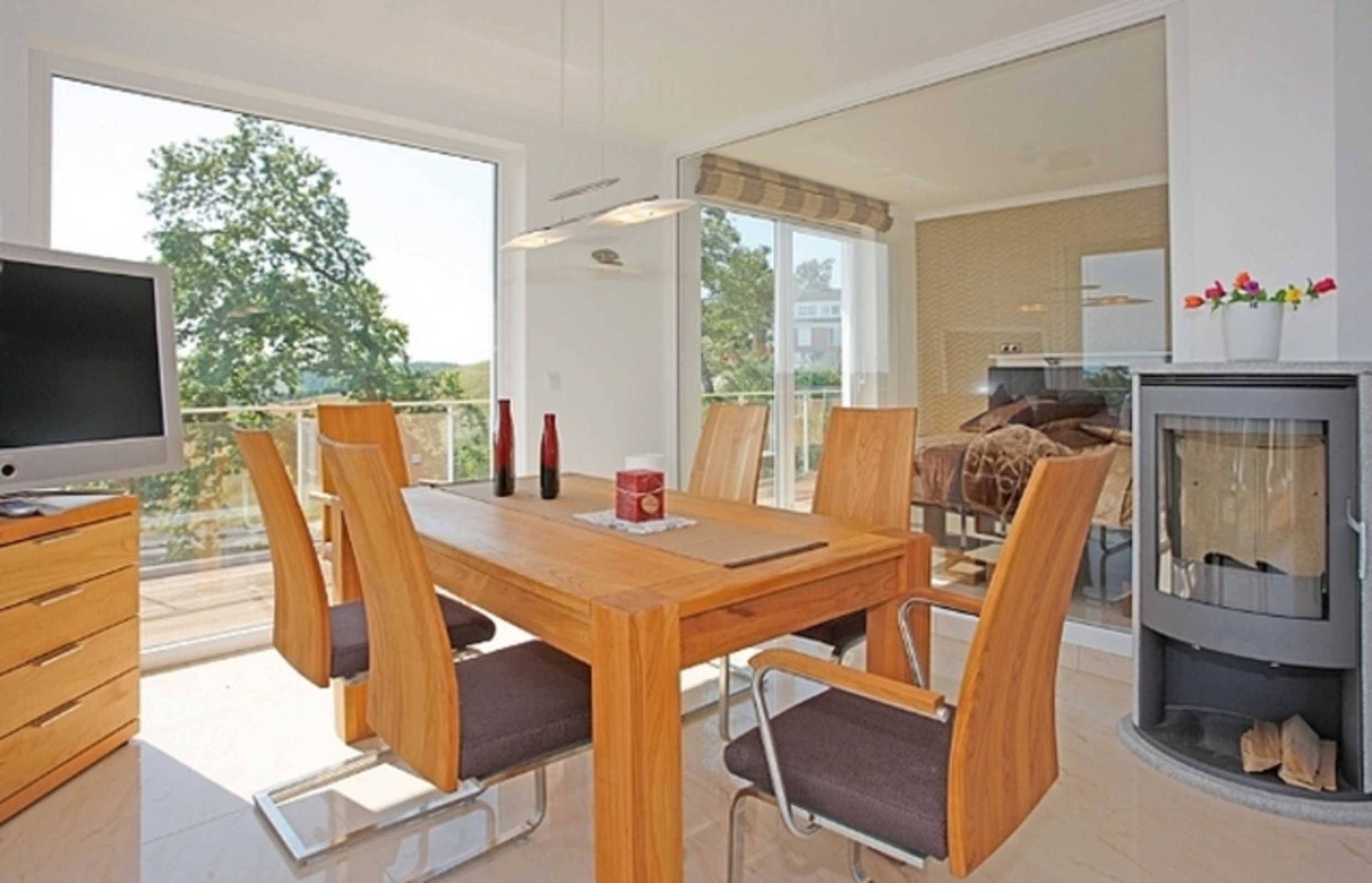 A modern dining area with a wooden table and chairs, a television, and a fireplace.