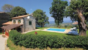 Une maison en pierre avec une piscine, entourée de haies et d’arbres bien entretenus.