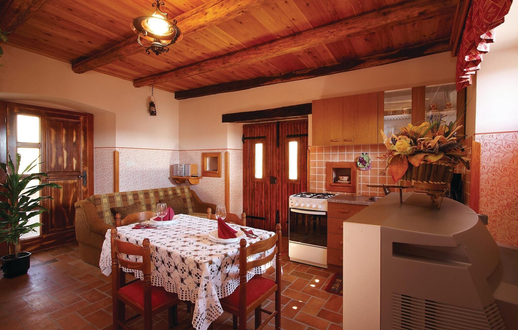 A cozy dining area with a wooden ceiling, a table set for two, and a kitchen with a gas stove and a grill.