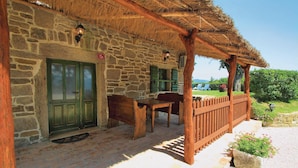Un bâtiment en pierre avec un toit de chaume, un banc en bois et une table à l’extérieur.