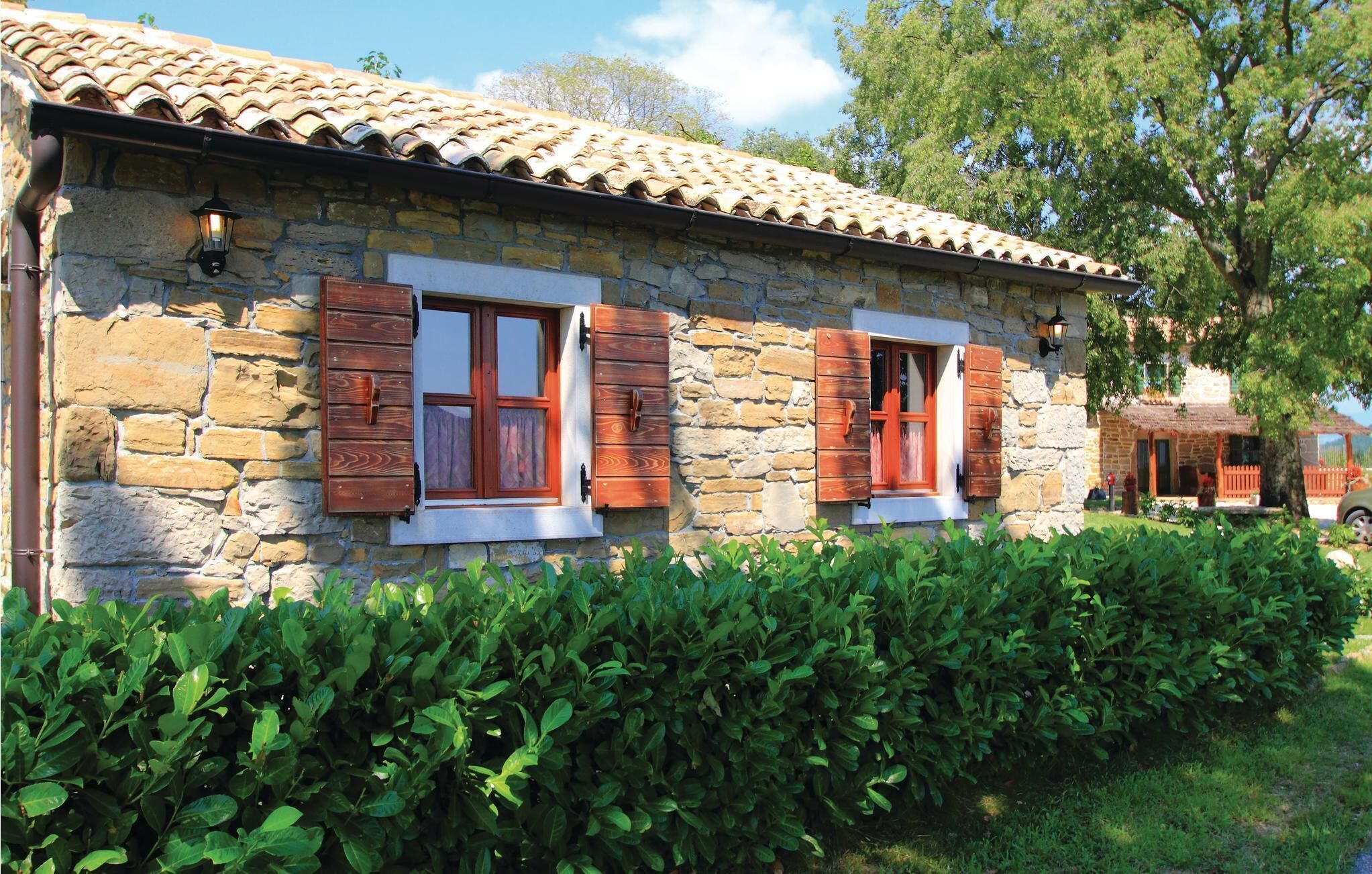 Un bâtiment en pierre avec des volets en bois, un toit en tuiles et une haie bien entretenue à l’avant.