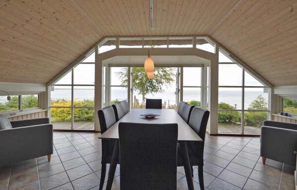 A dining area with a large table and chairs, large windows offering a view of the sea, and a hanging light fixture.