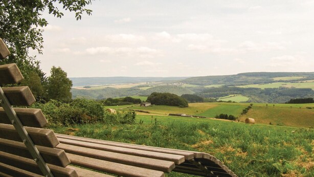 A wooden bench overlooking a rural landscape with rolling hills and fields.