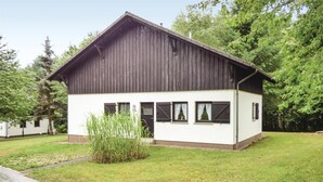A two-story wooden house with a white lower section, surrounded by greenery.