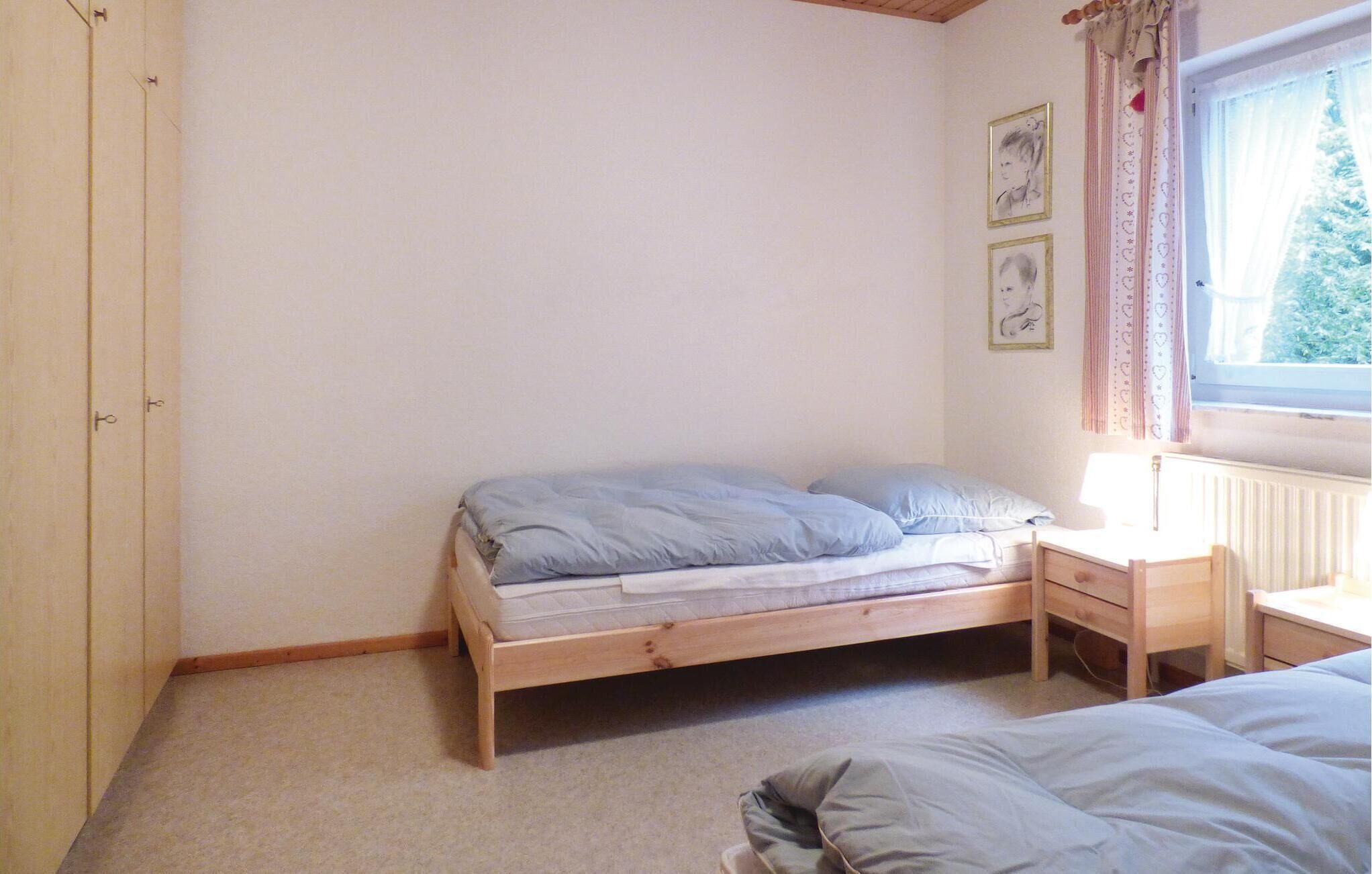 A small, simple bedroom with a single bed, a nightstand, and a window with curtains.