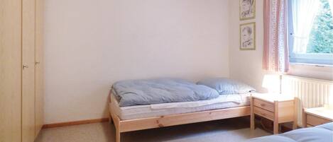 A small, simple bedroom with a single bed, a nightstand, and a window with curtains.