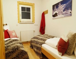 A room with two beds, a window, a radiator, a painting, and a red towel on a hook. - Vacation apartment for 7 people - Alpenjuwel (Laimach)