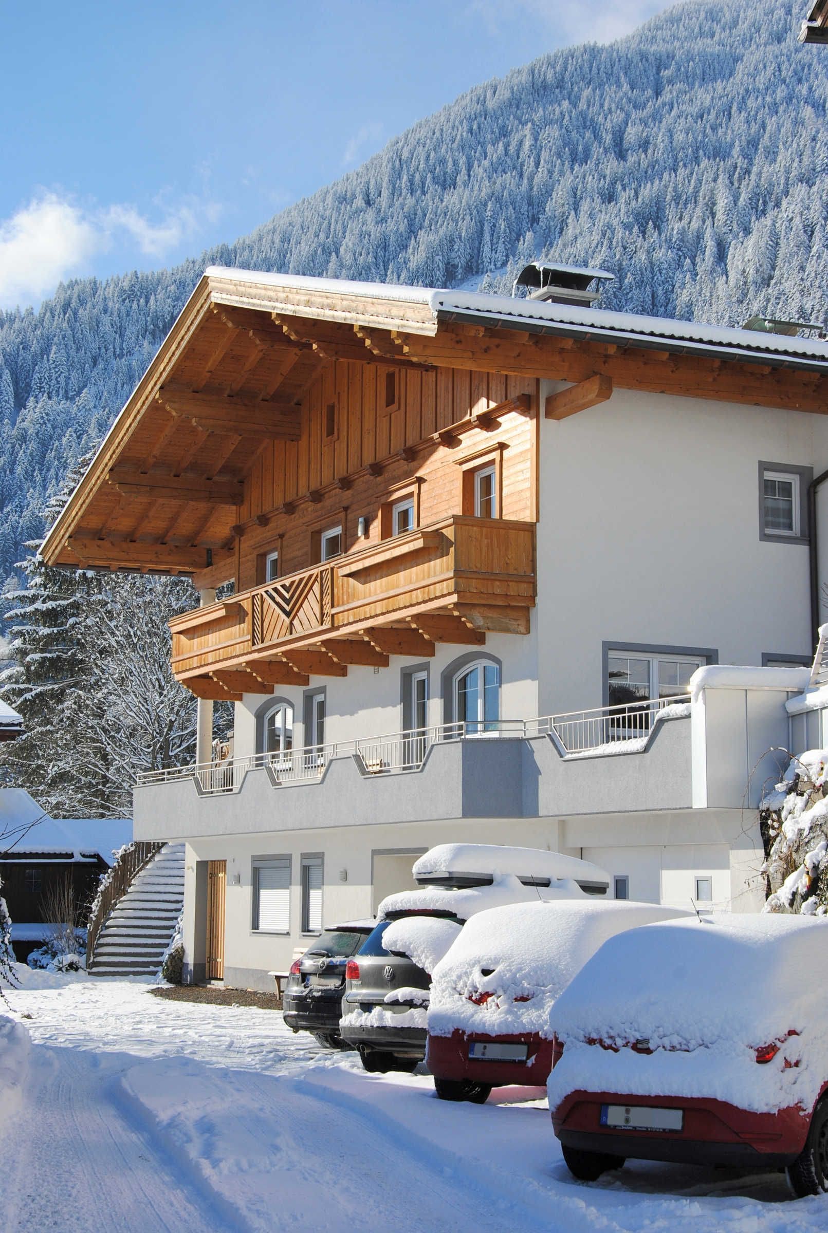 A multi-story building with a wooden balcony, a snow-covered mountain in the background, and parked cars.
