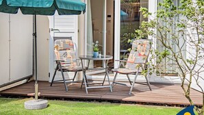 An outdoor patio with a table and two chairs, a green umbrella, and a potted plant. - Forum Marinar, Whg. 02 - Forum Marinar, Whg. 02 (Heringsdorf)