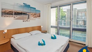 A hotel room with a large bed, a wooden headboard, and a view of the outdoors through large windows. - Forum Marinar, Whg. 02 - Forum Marinar, Whg. 02 (Heringsdorf)