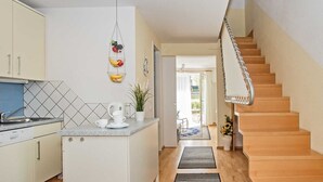 A modern kitchen with a central island, a dining area with a table and chairs, and a wooden staircase leading to an upper floor. - Forum Marinar, Whg. 02 - Forum Marinar, Whg. 02 (Heringsdorf)