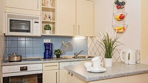 A kitchen with a microwave, coffee maker, sink, and cabinets. There are hanging baskets with fruits and a potted plant. - Forum Marinar, Whg. 02 - Forum Marinar, Whg. 02 (Heringsdorf)