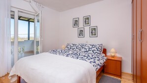 Una camera da letto con un letto, un comodino, un armadio in legno, una porta vetrata scorrevole su un balcone e quattro quadri appesi al muro.
