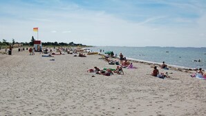 A beach with people sunbathing and swimming, a lifeguard tower, and a flag. - Awesome home in Karrebæksminde with sauna (Karrebæksminde)