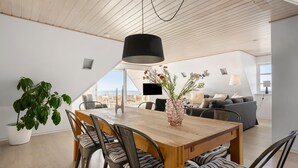 Ein moderner Essbereich mit Holztisch und -stühlen, einer Topfpflanze und Meerblick.