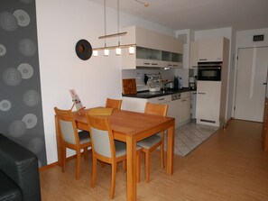 Une cuisine moderne avec des meubles blancs, un four noir et un coin repas comprenant une table et des chaises en bois.