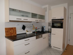 A modern kitchen with white cabinets, a black countertop, a Siemens oven, and a sink.