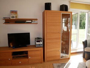 Een woonkamer met een televisie, een houten tv-meubel en een vitrinekast met glazen deuren.