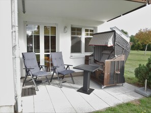 Une terrasse avec deux chaises à rayures, une petite table et un barbecue.