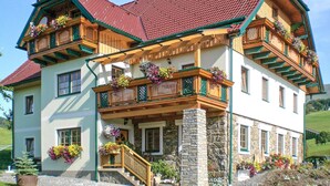 Ein zweistöckiges Haus mit einem Steinfundament, hölzernen Balkonen mit Blumenkästen und einem roten Ziegeldach.