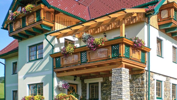Ein zweistöckiges Gebäude mit rotem Ziegeldach, hölzernen Balkonen mit grünen Akzenten und Blumenkästen.