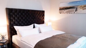 A neatly made bed with a tufted headboard, white bedding, and a brown throw blanket. - (179) 2-room apartment - Apartment house Waldhaus (Kühlungsborn)
