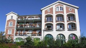 A multi-story hotel with balconies, a central courtyard, and a mix of brick and white exterior. - (179) 2-room apartment - Apartment house Waldhaus (Kühlungsborn)