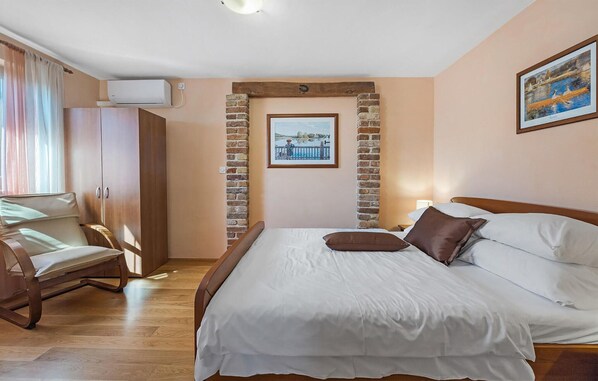 A bedroom with a wooden bed, a chair, a brick wall, and a picture of a landscape. - Cozy home in Visnjan with sauna (Visnjan)