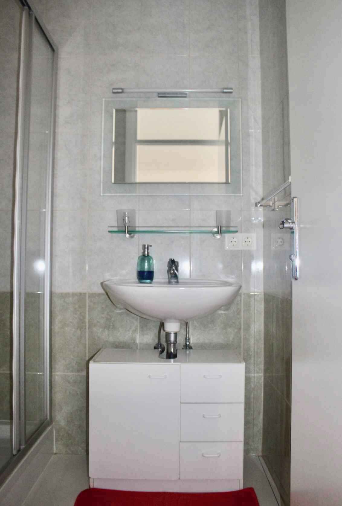 A bathroom with a white sink, a glass shelf above it, and a mirror.