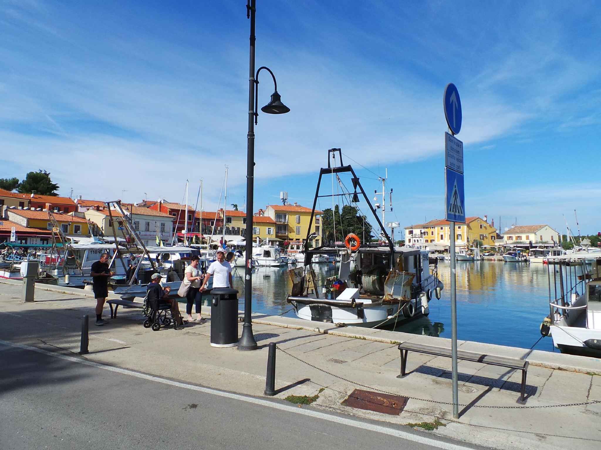 Un puerto deportivo con barcos amarrados, un paseo peatonal y edificios al fondo.