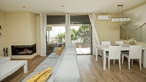 A modern living room with a sofa, dining table, and chairs. There is a fireplace and a large window with curtains. - Pet friendly home in Santa Susanna (Santa Susanna)
