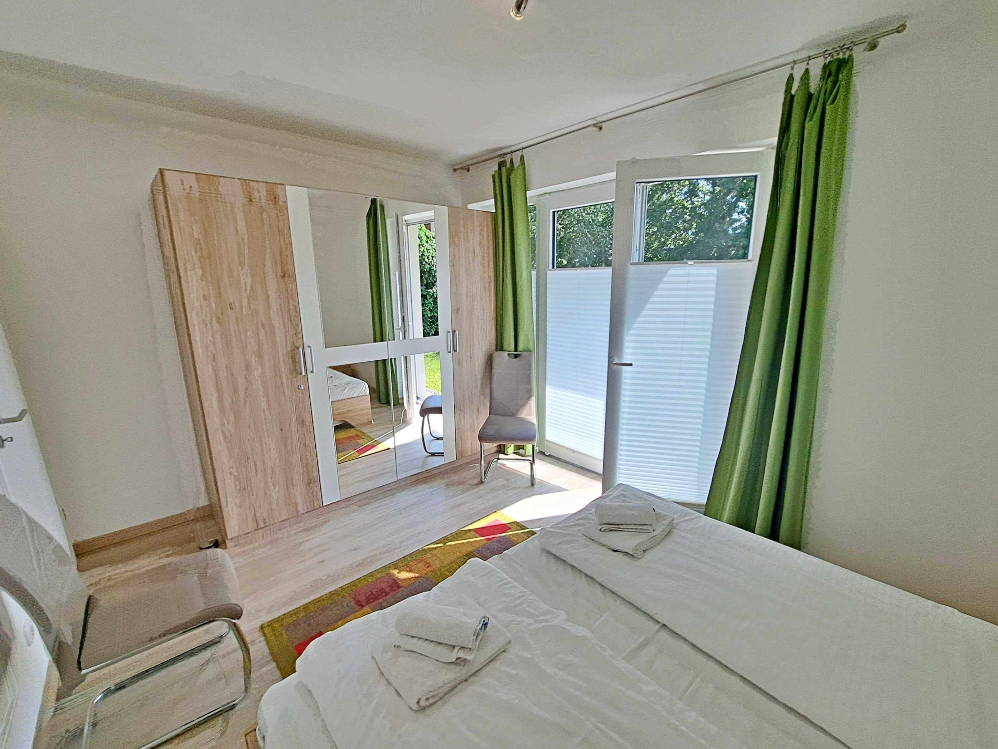 A bedroom with a bed, a chair, a wardrobe, and a sliding glass door leading to a balcony.