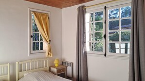Une chambre avec un lit, une table de chevet avec une lampe, une fenêtre avec des rideaux et un radiateur.